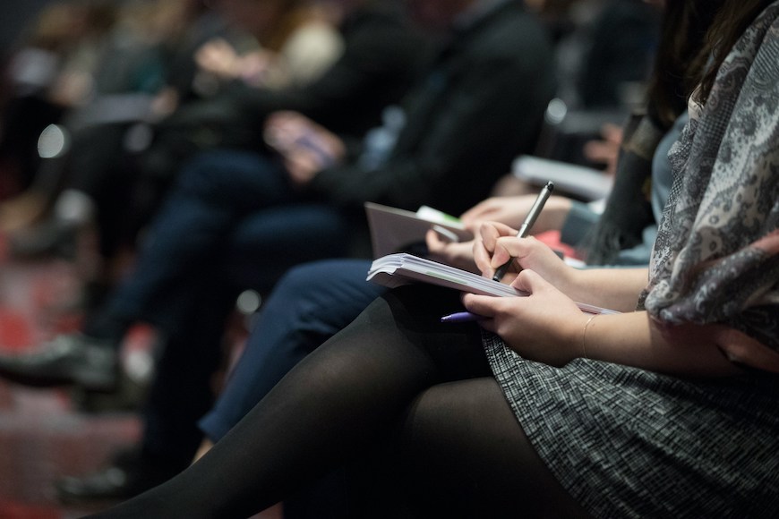 Student journalist taking notes in the front row of a lecture hall