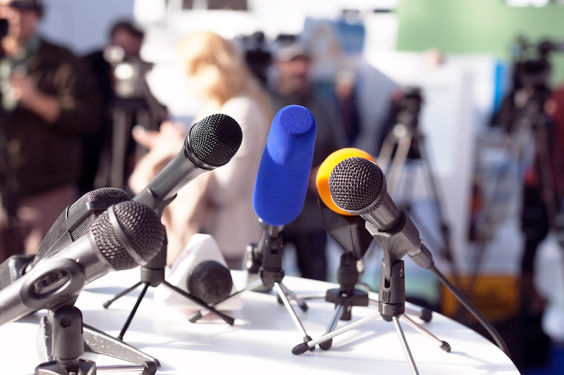 Microphones gathered on a table at a media scrum